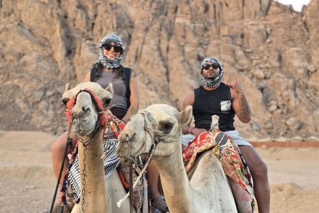 Two guests riding camels below the rocky mountains of the Sinai desert near Sharm El Sheikh