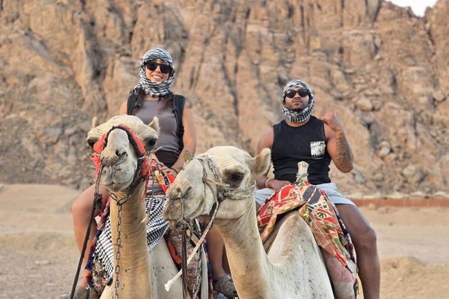 Two guests riding camels below the rocky mountains of the Sinai desert near Sharm El Sheikh